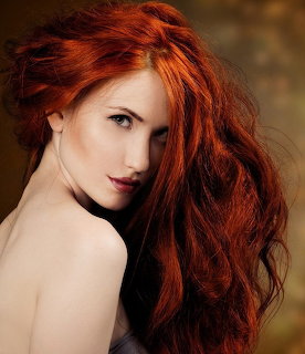 Woman with long wavy red hair looking over her bare shoulder against a dark background