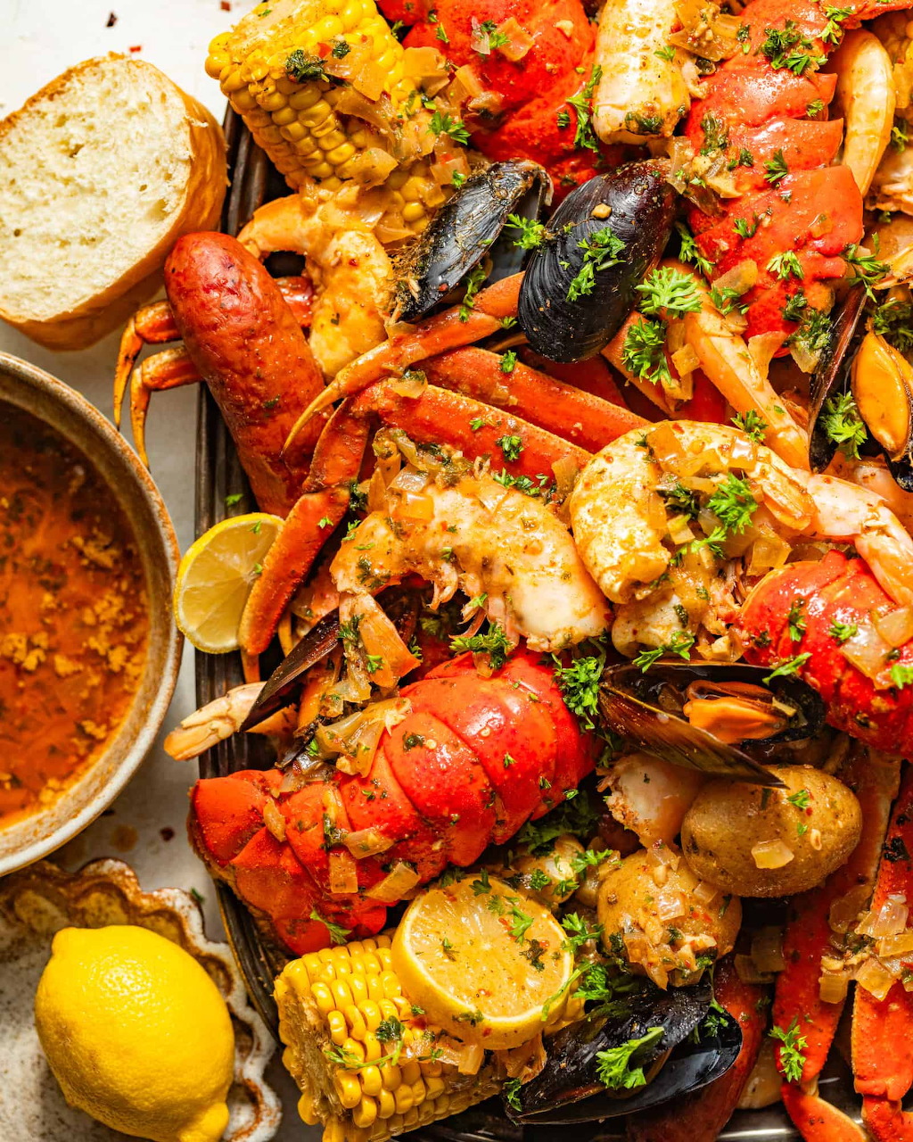 Overhead view of seafood boil with lobster, shrimp, corn, mussels, potatoes, sausage, lemon wedges, and dipping sauce