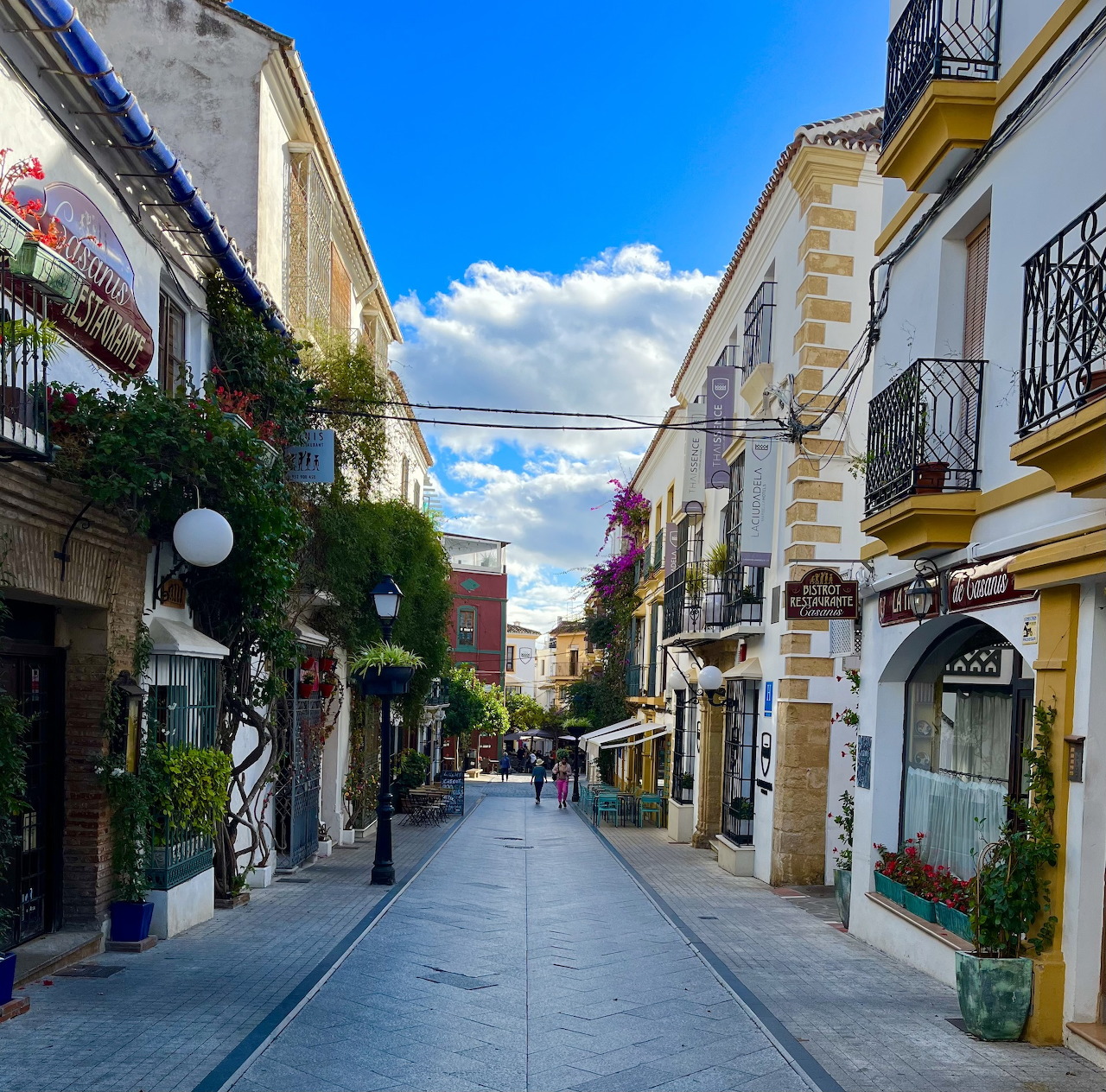 Narrow pedestrian street in Marbella old town with white buildings, flowers, and blue sky