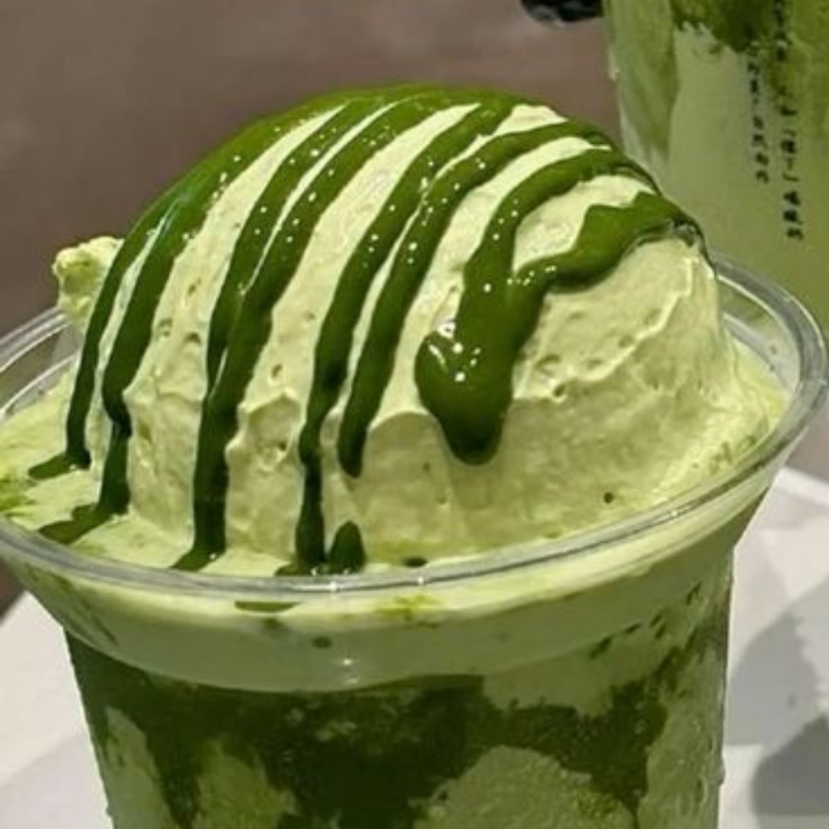 Close-up of matcha ice cream in a clear cup topped with dark green syrup