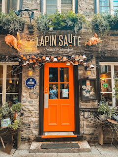 Orange restaurant entrance with stone walls, wooden rabbit sign, and decorative plants