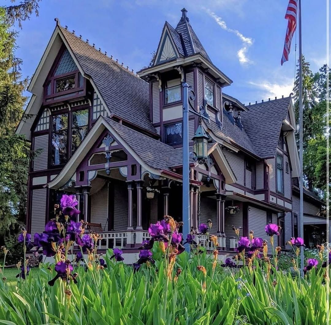 Victorian house with purple irises blooming in front garden, American flag on porch, blue sky background