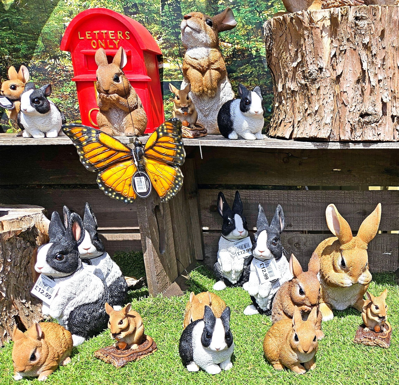 Rabbit figurines displayed on grass and wooden shelves with a red mailbox and butterfly ornament