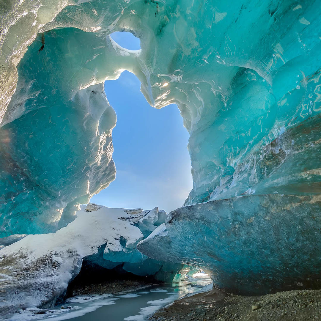 Blue ice cave inside Mendenhall Glacier with sky opening, snow, and meltwater