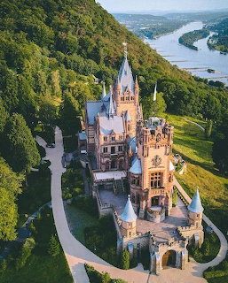 Aerial view of Drachenburg Castle with towers surrounded by green forests and river in Germany