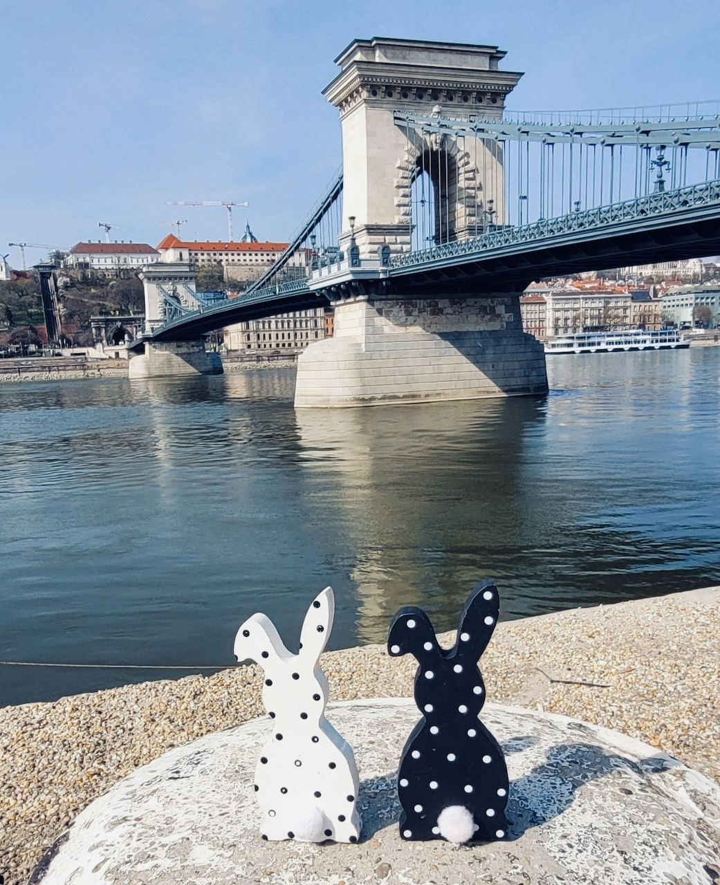 White and black polka-dot Easter bunny figurines on stone ledge overlooking Chain Bridge and Danube River in Budapest