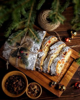 Sliced Christmas stollen dusted with powdered sugar on wooden cutting board with evergreen branches and holiday decorations