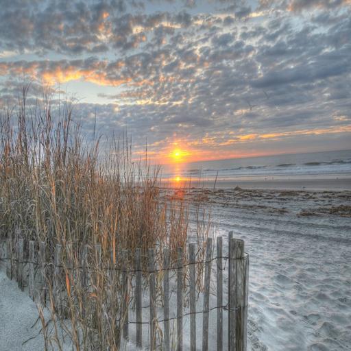 Golden sunrise over Myrtle Beach with dune fence, sea oats, and dramatic clouds reflected on wet sand