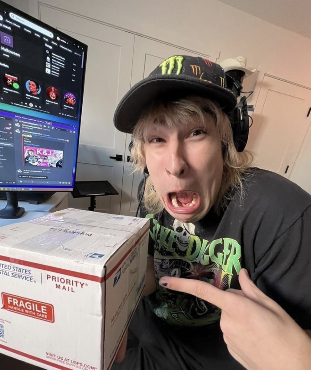 Young man with blonde hair and Monster Energy hat making a surprised face next to a fragile shipping box