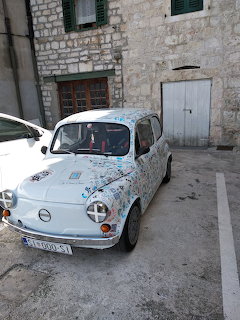 White vintage Fiat 500 parked on cobblestone street in front of old stone building