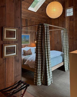 Rustic cabin bedroom with four-poster canopy bed, plaid curtains, wooden walls, and paper lantern