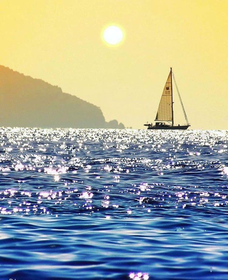 Sailboat sailing on shimmering water at sunset with mountain silhouette