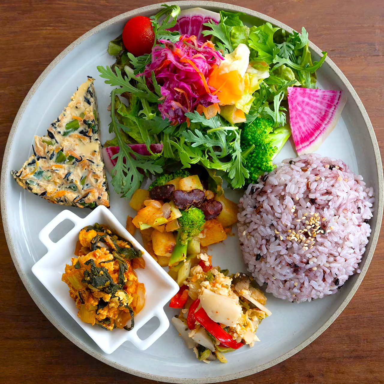 Overhead view of a healthy lunch plate with salad, purple rice, grilled vegetables, and crackers