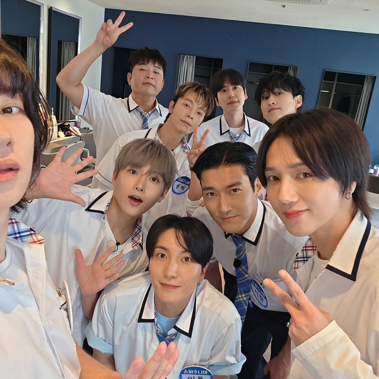 Group selfie of Super Junior members indoors wearing white shirts and ties