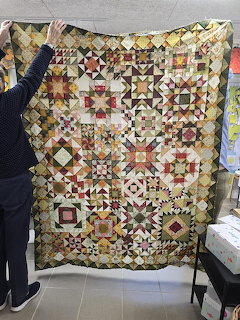 Traditional sampler quilt with geometric patchwork blocks in warm colors held up for display