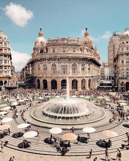 Large circular fountain in Piazza De Ferrari, Genoa with historic palace buildings and crowds