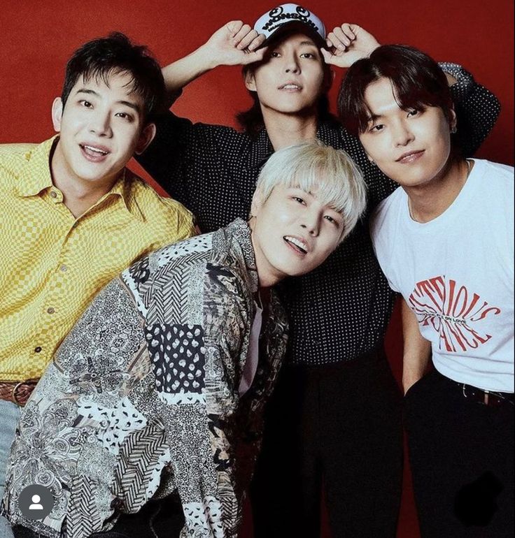 Four young men posing together in front of a red background