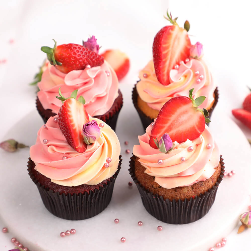Four chocolate cupcakes with pink frosting and fresh strawberries