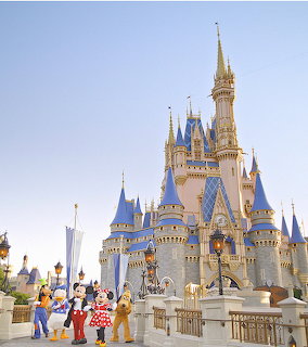 Cinderella Castle with blue and gold spires, Disney characters including Mickey Mouse in front, clear blue sky