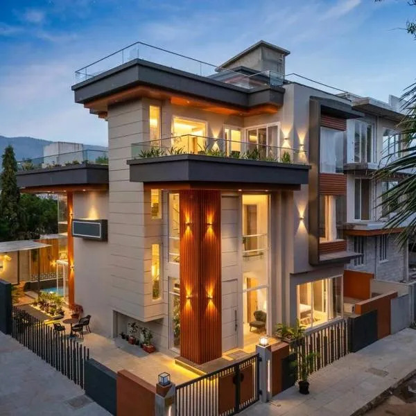 Modern multi-story mansion with lit windows, balconies, and a gated entrance at dusk