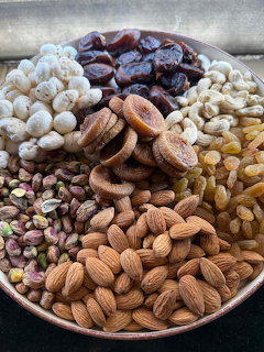 Round platter with assorted dry fruits and nuts including almonds, pistachios, raisins, cashews, and dried apricots