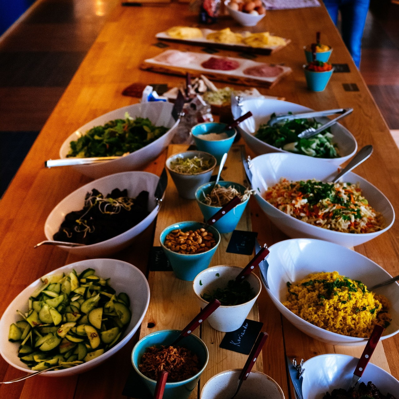 Overhead view of multiple Indian vegan dishes arranged on wooden table with various bowls containing curries and vegetables