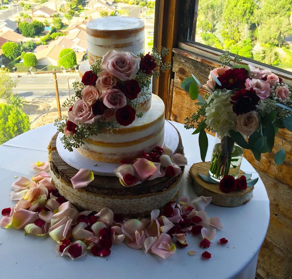 Three-tier wedding cake with pink roses and calla lilies on white table by sunny window