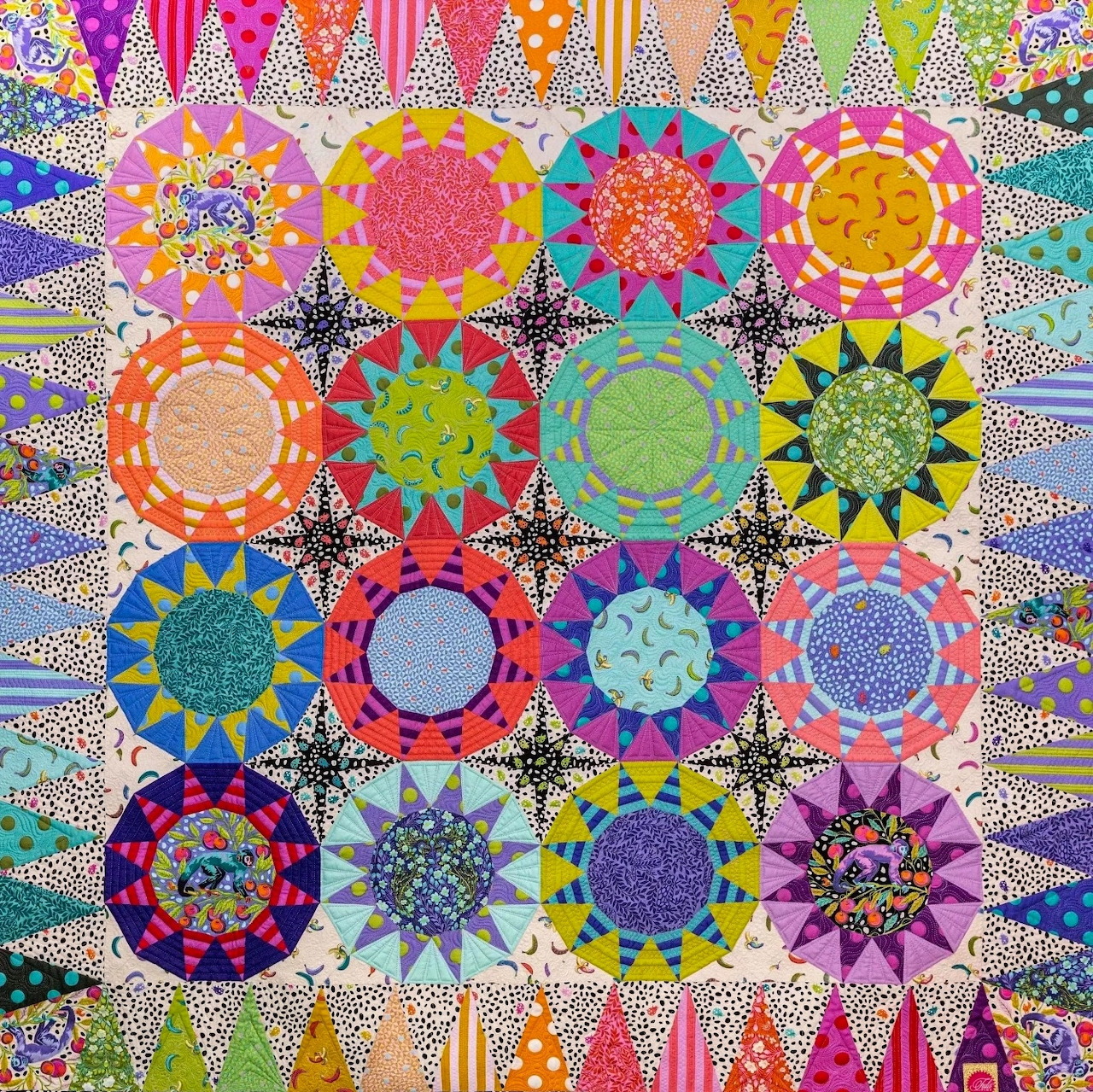 Colorful quilt with 16 circular mandala patterns in rainbow hues on geometric patterned background