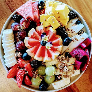 Colorful platter with sliced fruit, cheese, granola, and toast on a round plate