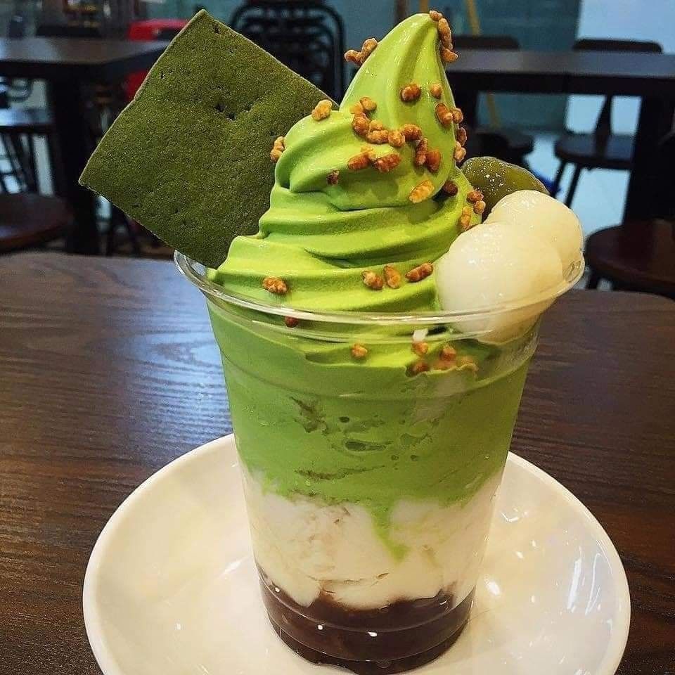 Matcha green tea soft serve sundae topped with gold crunchies, mochi, and a green wafer in a cafe