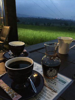 Coffee cups and a glass server on a table overlooking a green field at dusk