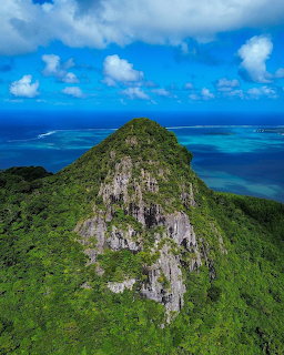 Aerial view of green mountain peak with ocean and islands below blue sky