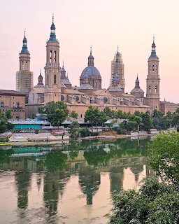 Basilica del Pilar with multiple towers reflected in river water at sunset