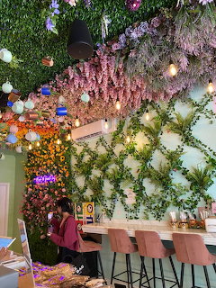Café interior with lush flower and plant decorations covering walls and ceiling, pink seating along counter