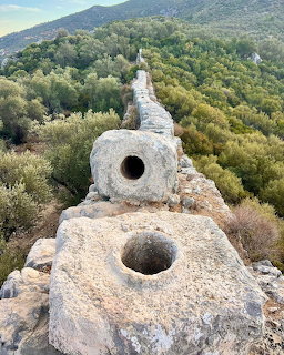 Ancient stone aqueduct with round holes extending across a forested hillside in Turkey