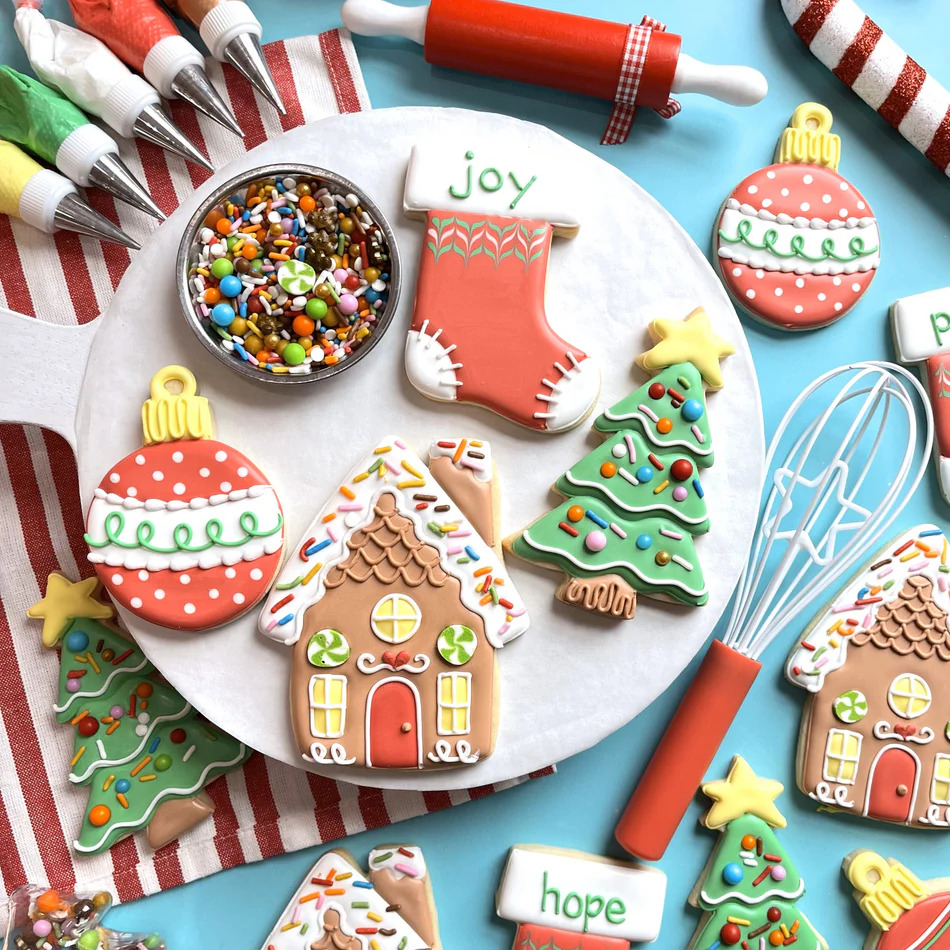 Christmas cookies on a white plate with sprinkles, whisk, piping bags, and striped cloth