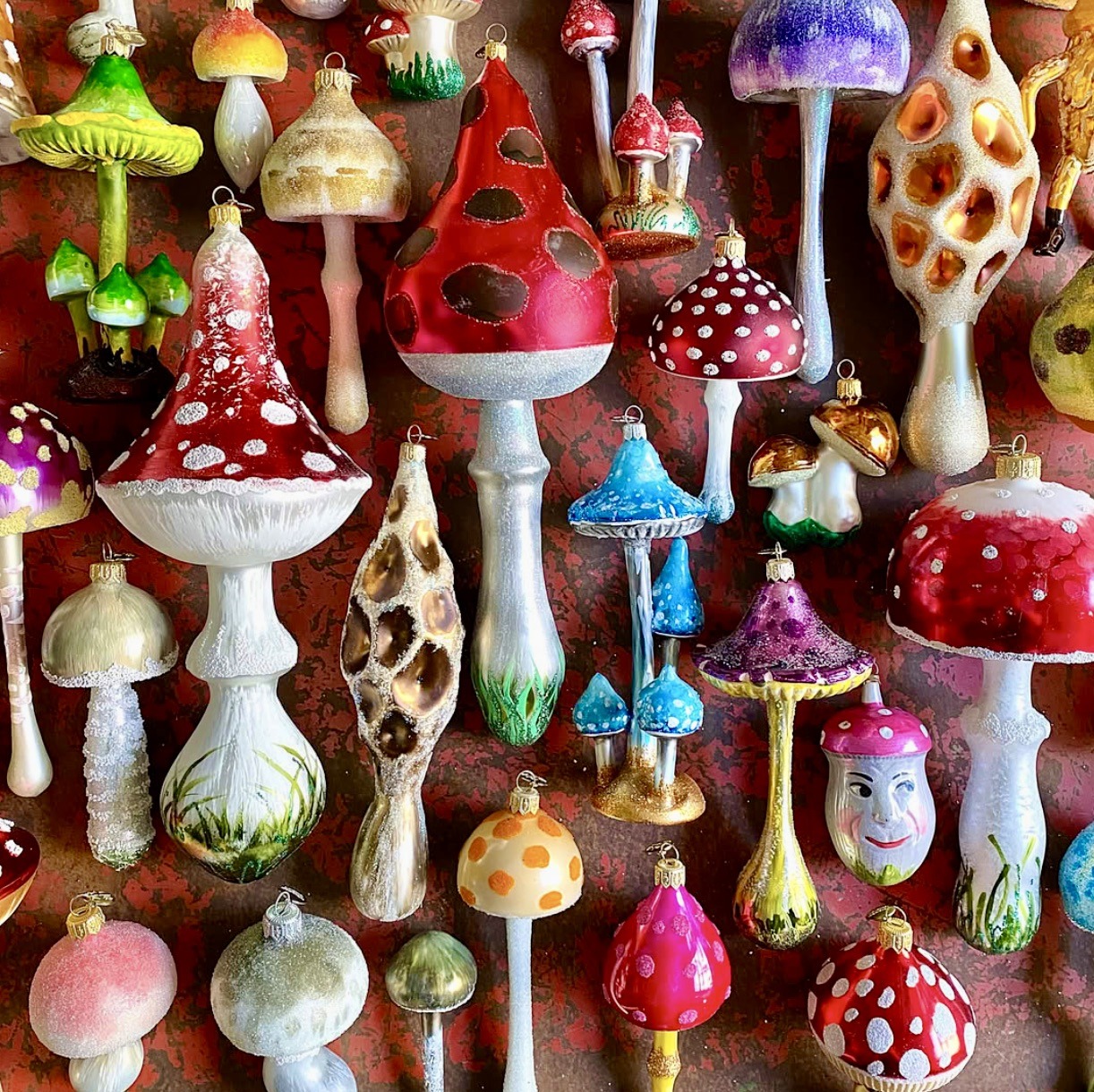 Collection of colorful glass mushroom ornaments with spotted caps and decorative stems arranged on wood background
