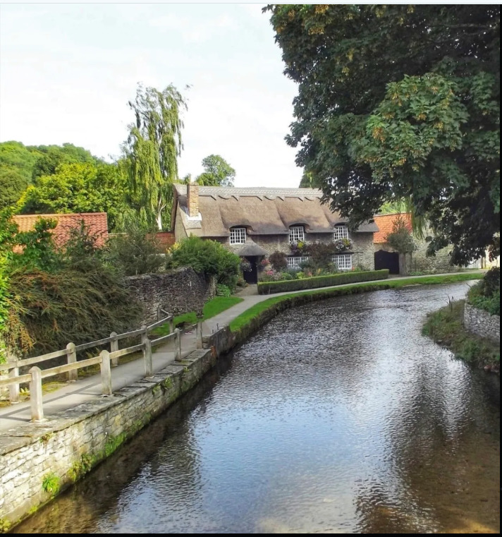 Thatched roof cottage beside tranquil canal with wooden fence and trees