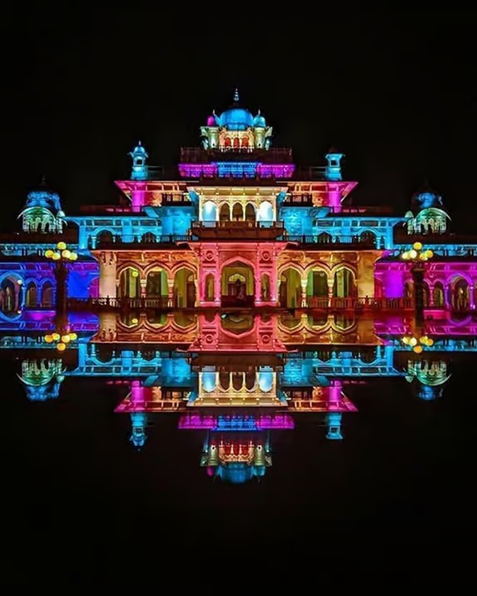 Albert Hall Museum lit in bright colors at night with a mirror-like reflection on black
