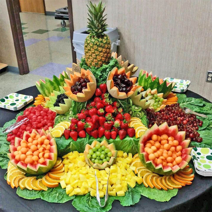 Decorative fruit buffet with carved watermelons, pineapple, strawberries, grapes, and cantaloupe on a black table