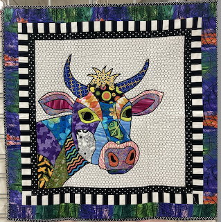Handmade quilt with colorful patterned cow on cream background, surrounded by checkered and floral border