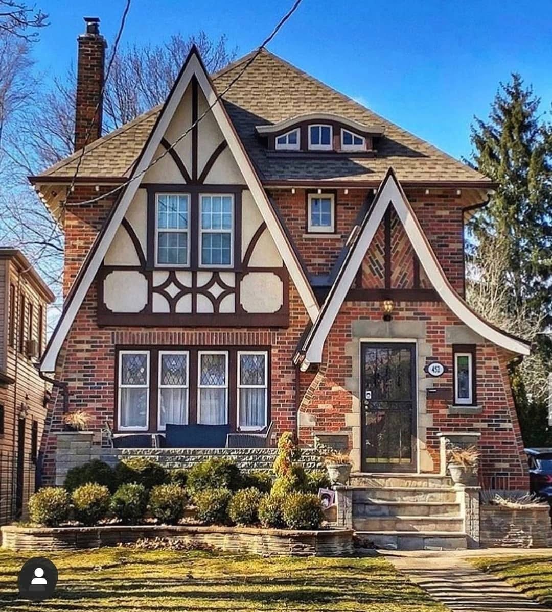 Tudor-style red brick house with pointed gables, decorative half-timbering, and landscaped front yard