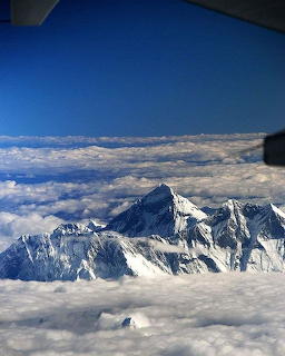 Snow-covered mountain peak above clouds seen from an airplane window