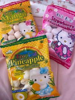Three bags of tropical fruit-flavored marshmallows in mango, pineapple, and strawberry on pink background