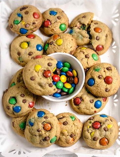 Homemade cookies with colorful M&M candies arranged in a circle around a bowl of M&Ms on white marble