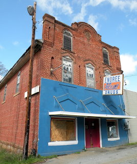 Abandoned two-story red brick building with blue storefront and Enoree Drugs sign