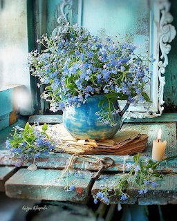 Blue forget-me-not flowers in a blue ceramic vase on a rustic turquoise wooden shelf with a candle