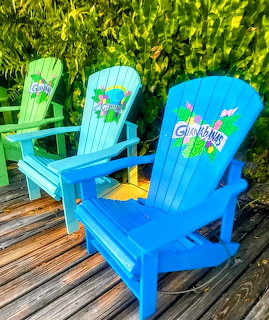 Blue and turquoise painted Adirondack chairs with floral artwork on a wooden deck