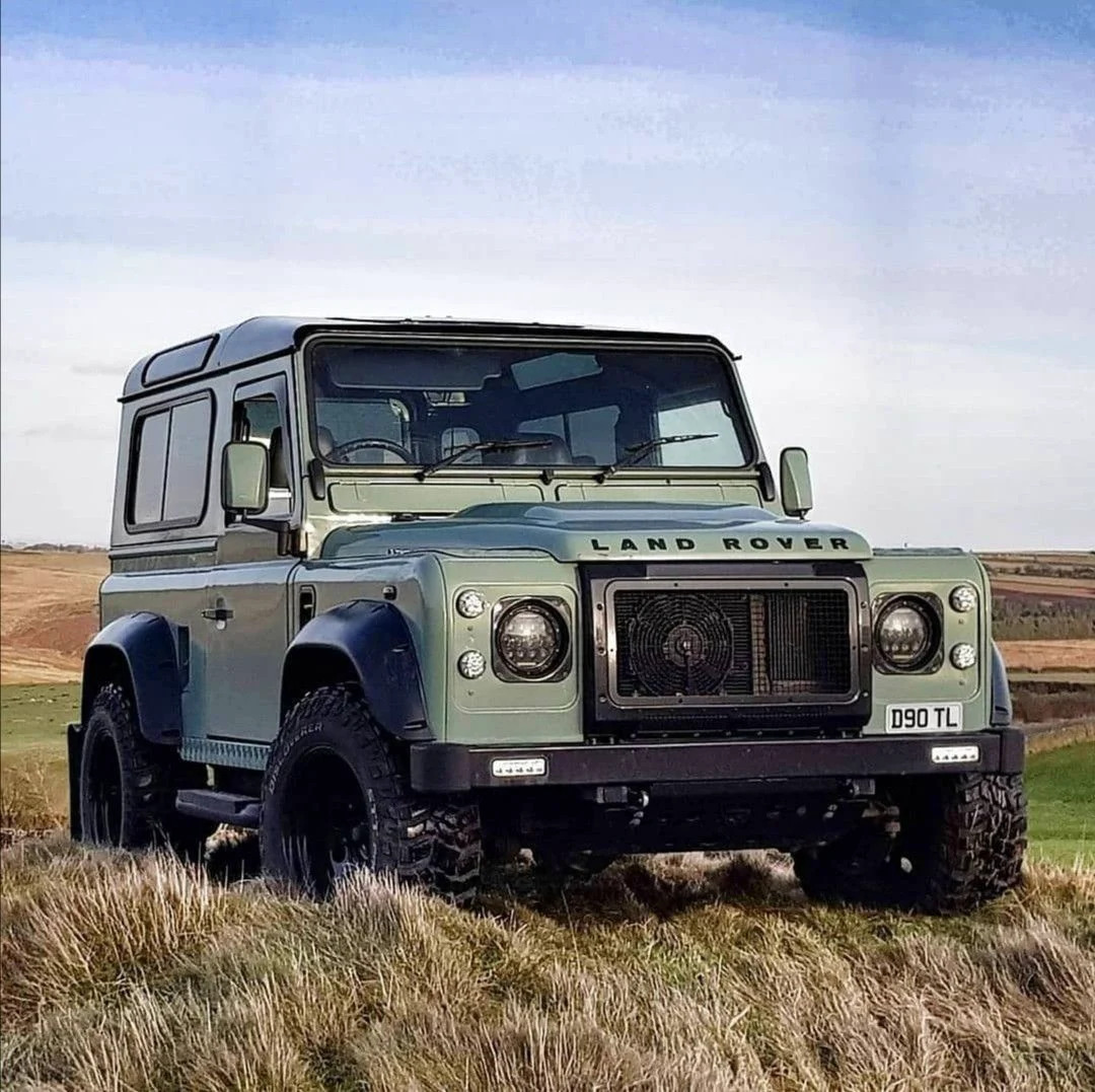 Classic Land Rover Defender parked in a grassy field under a cloudy sky
