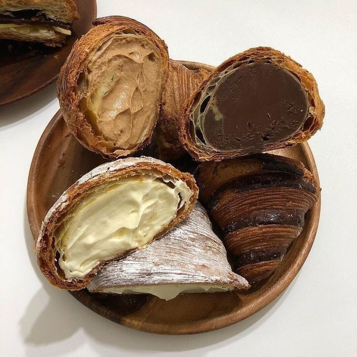 Four croissants with chocolate and cream fillings on a wooden plate